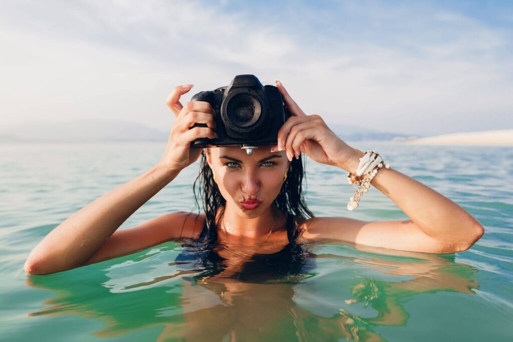 beautiful-sexy-woman-tanned-skin-black-bikini-swimsuit-standing-blue-water-holding-digital-photo-camera-hot-tropical-summer-vacation-fashion-trend-flirty-wet