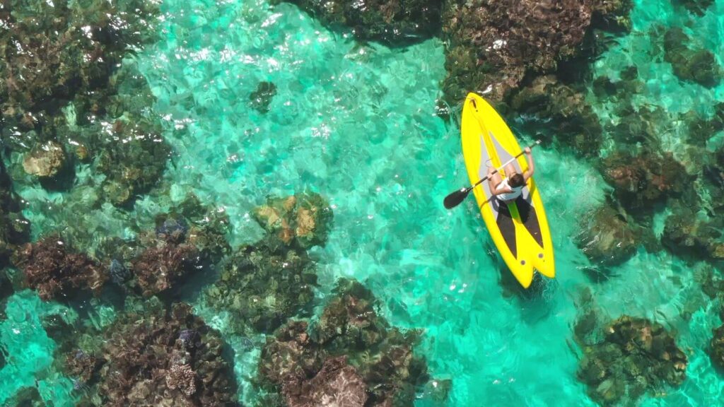 woman-paddle-boarding-tropical-water-near-reefs-aerial-view