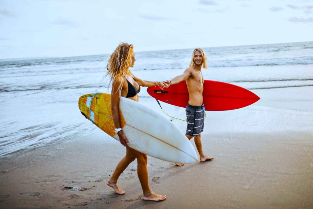 couple-holds-hands-onandaman-beach-with-surfboards