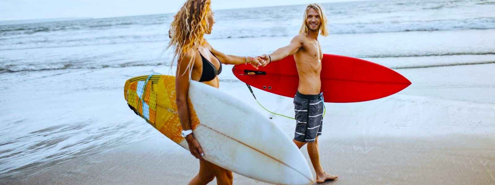 couple-holds-hands-onandaman-beach-with-surfboards