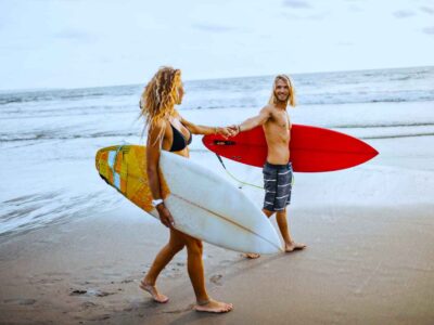 couple-holds-hands-onandaman-beach-with-surfboards